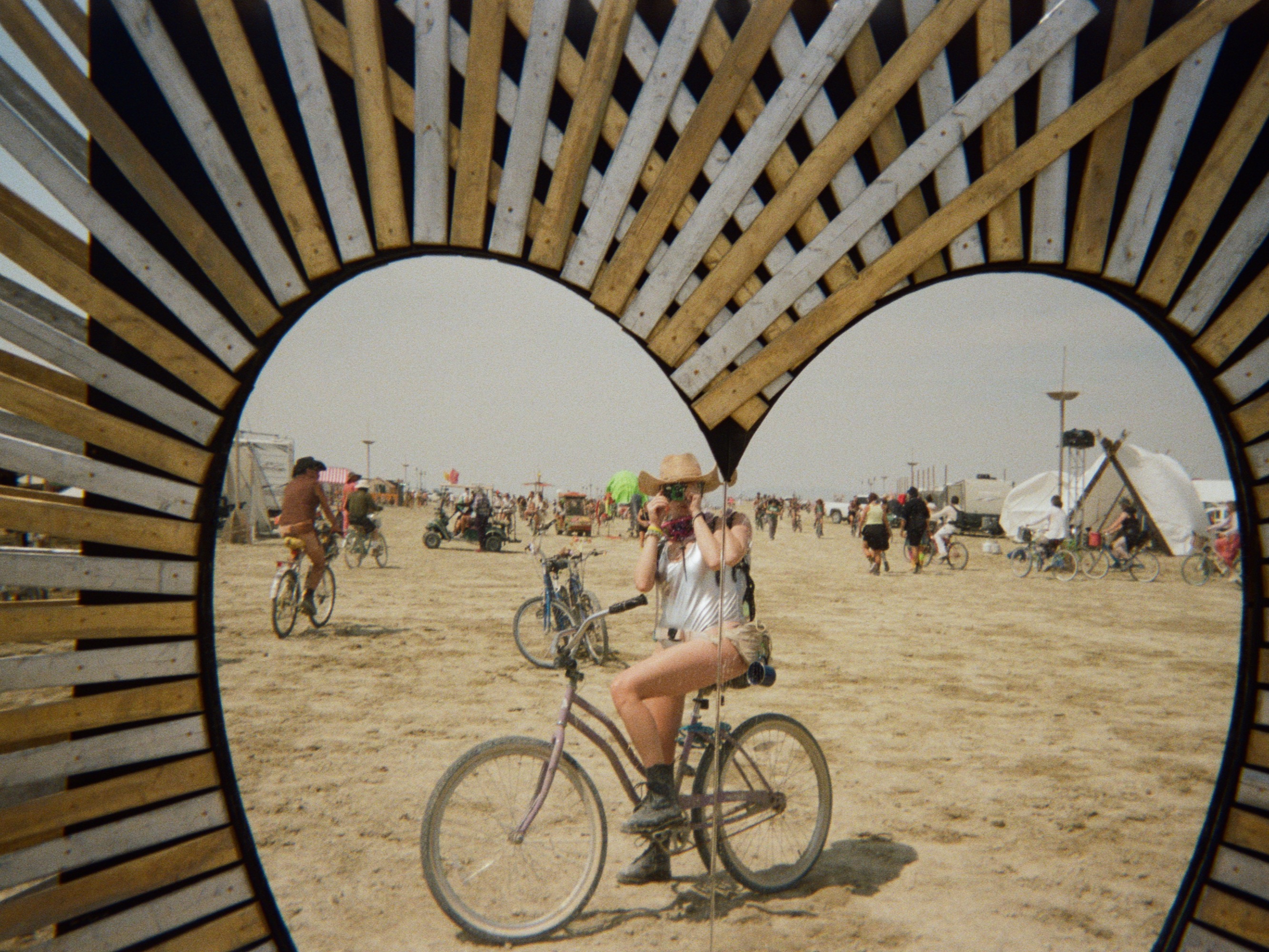 A heart-shaped wooden art installation, with a woman on a bicycle framed inside it